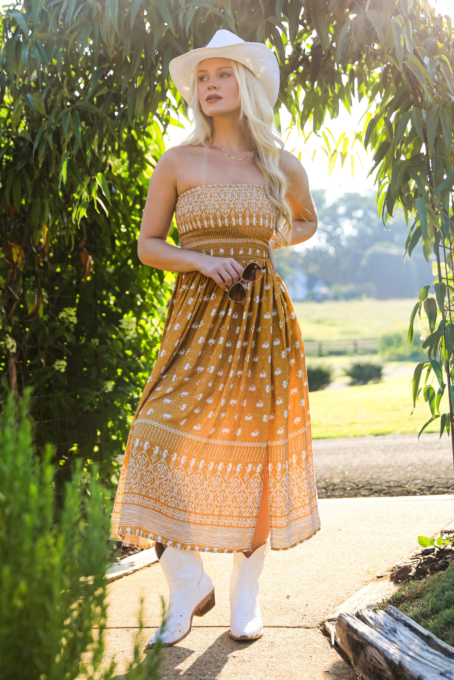 Woman in a patterned dress standing under a green archway with a scenic background
