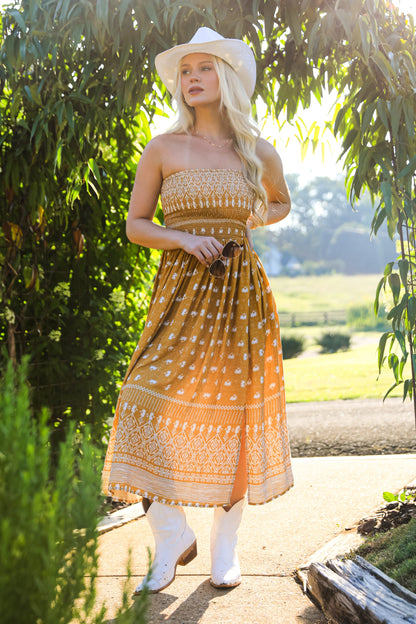 Woman in a patterned dress standing under a green archway with a scenic background