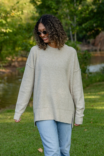 Woman wearing a beige sweater and sunglasses outdoors by a pond