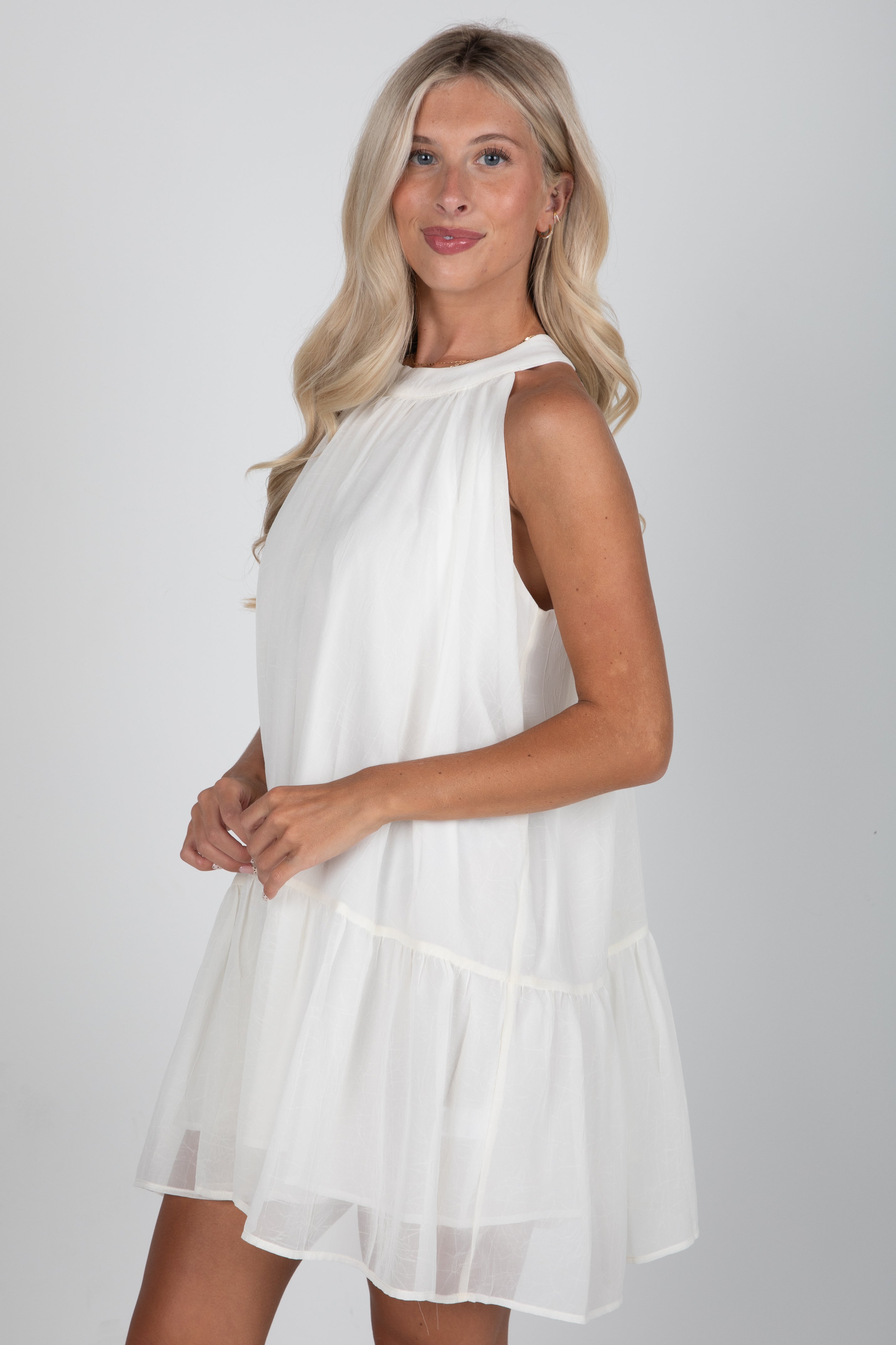 Woman wearing a white sleeveless dress against a plain background