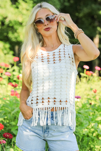Woman in a white fringe top and denim shorts standing in a field of flowers.