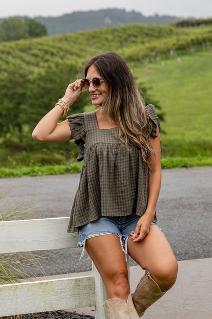 Woman in a plaid top and denim shorts standing in a vineyard.