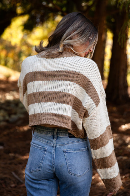 Person wearing a striped sweater and blue jeans standing in a forest