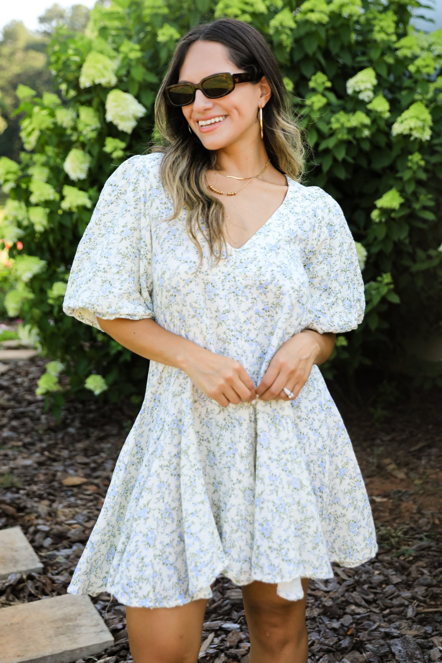 Woman wearing a floral dress standing outdoors with greenery in the background