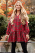 Woman in a red plaid dress standing in an urban park with autumn foliage.