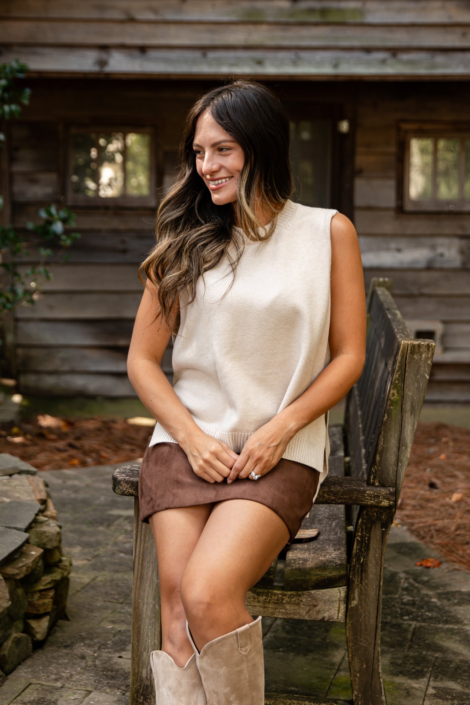 Woman sitting on a wooden bench outdoors with a rustic cabin in the background