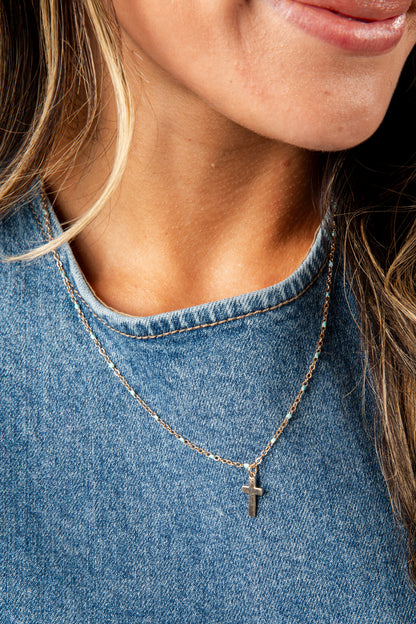 Close-up of a person wearing a silver necklace with a cross pendant on a blue denim background.