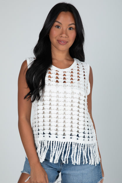 Woman wearing a white crochet top with fringe on a gray background