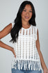Woman wearing a white crochet top with fringe details against a plain background