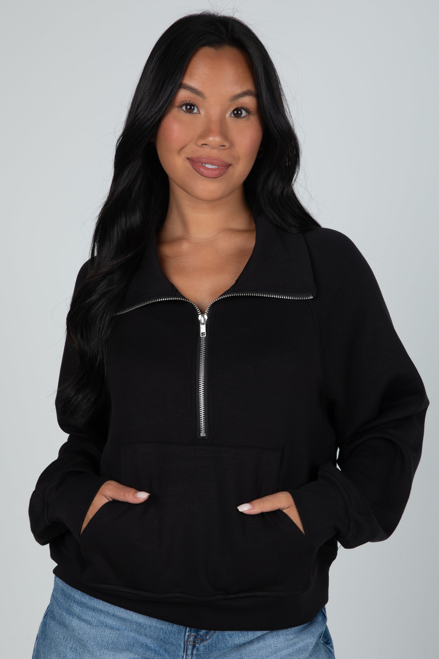 Woman wearing a black zip-up hoodie against a gray background