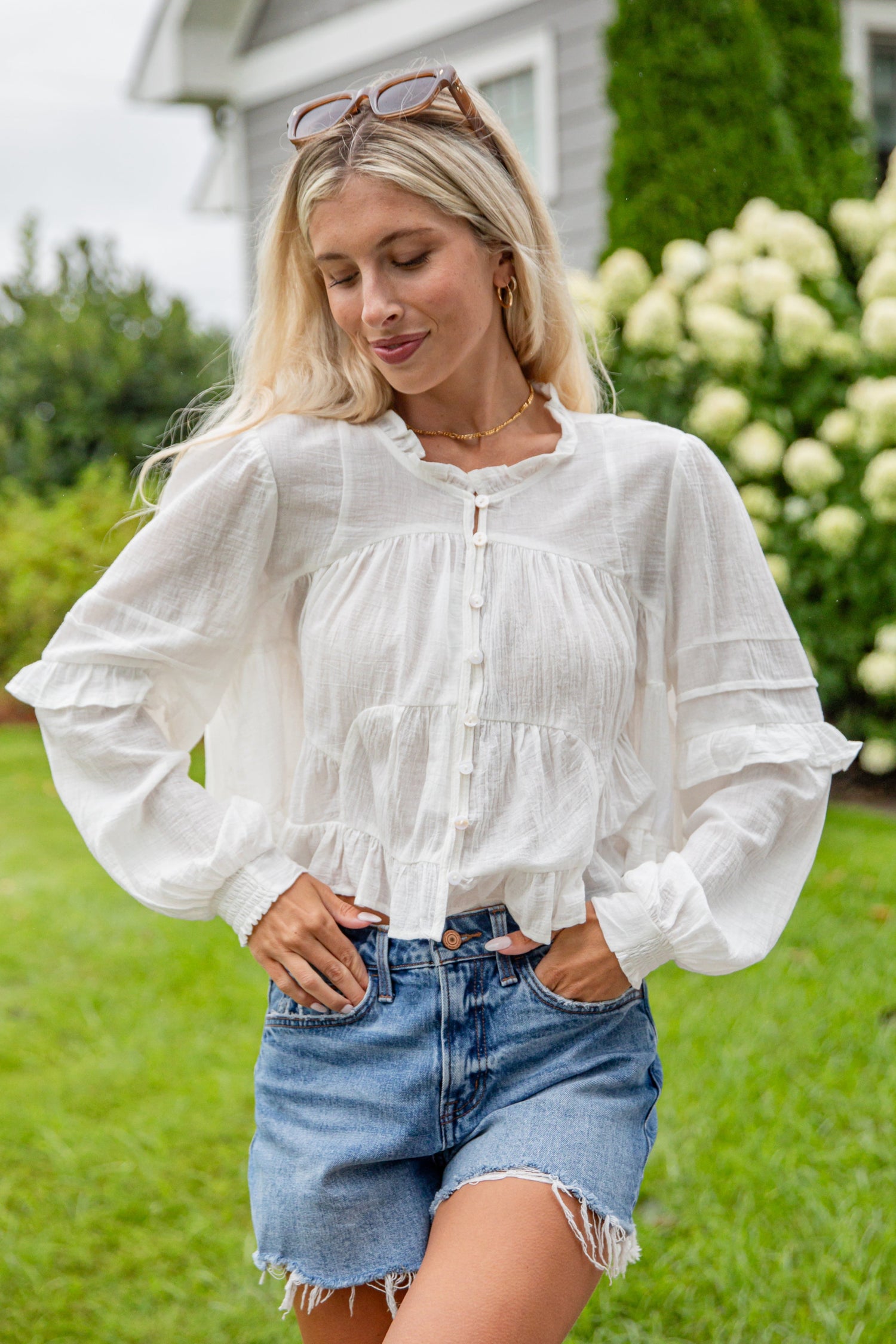 Woman wearing a white blouse and denim shorts standing outdoors.