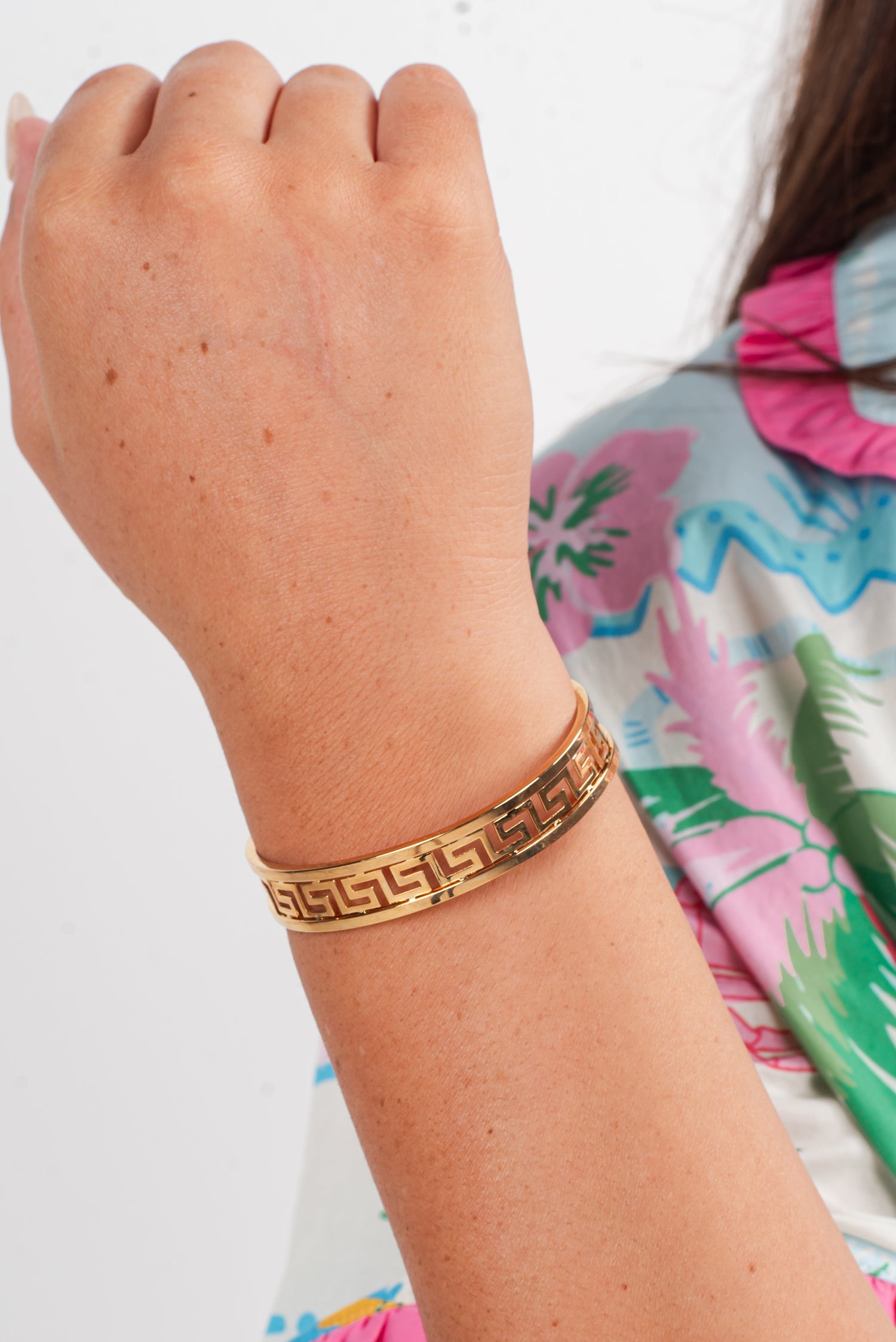 Gold bracelet on a wrist with a colorful background