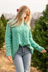 Woman in a teal sweater standing among Christmas trees