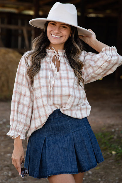 Woman wearing a plaid shirt, denim skirt, and white hat in a rustic setting.