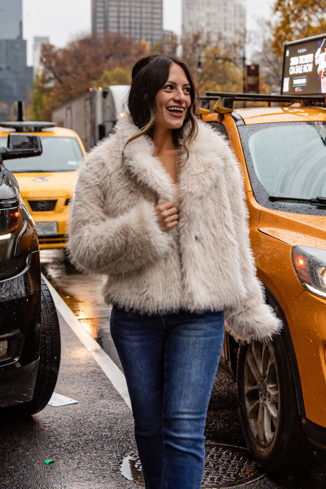 Woman in a fur coat walking in a city street with taxis in the background