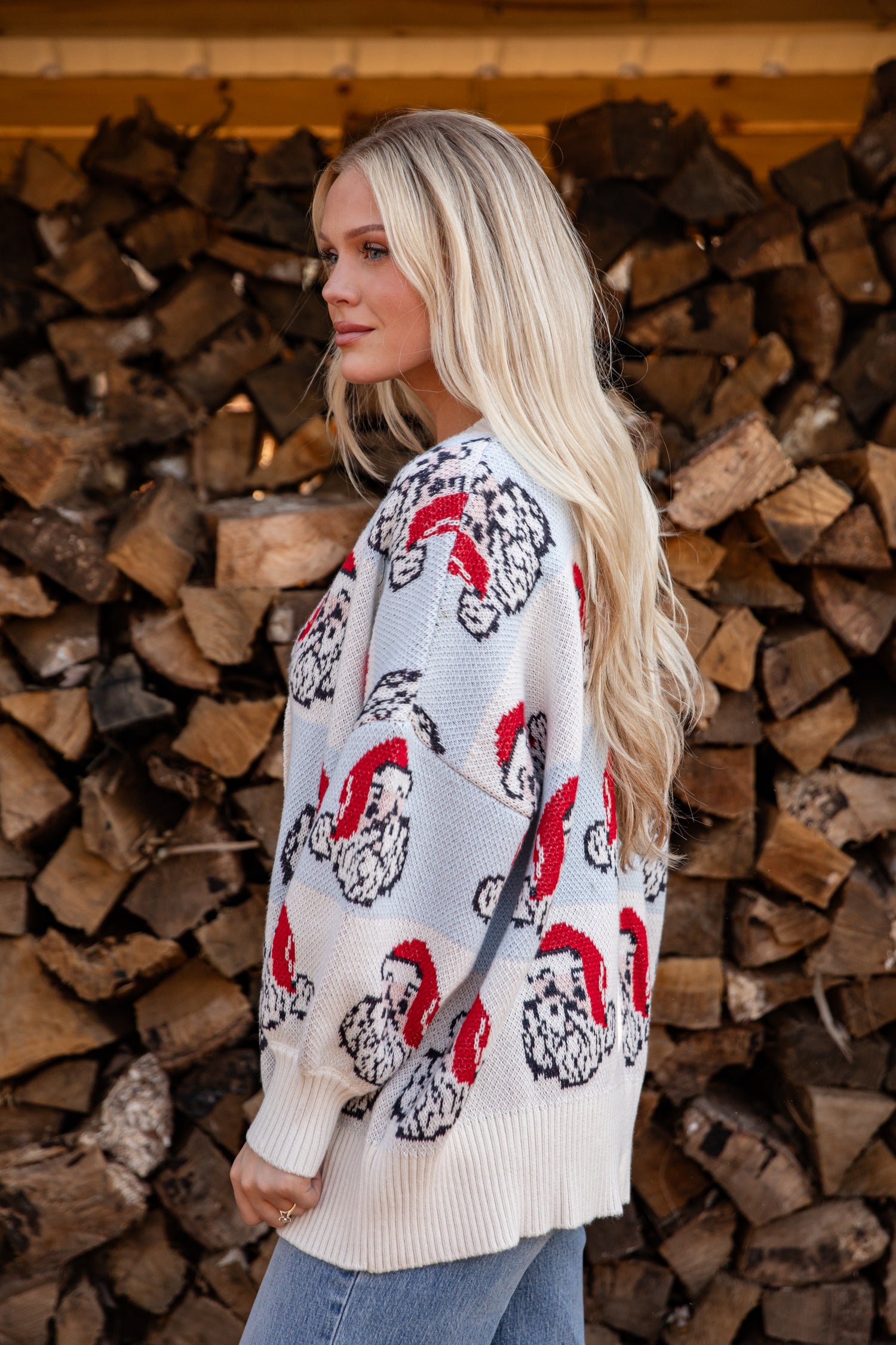 Woman wearing a patterned sweater standing in front of stacked firewood.