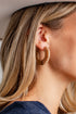 A close-up side profile of a woman wearing a textured, circular gold hoop earring.