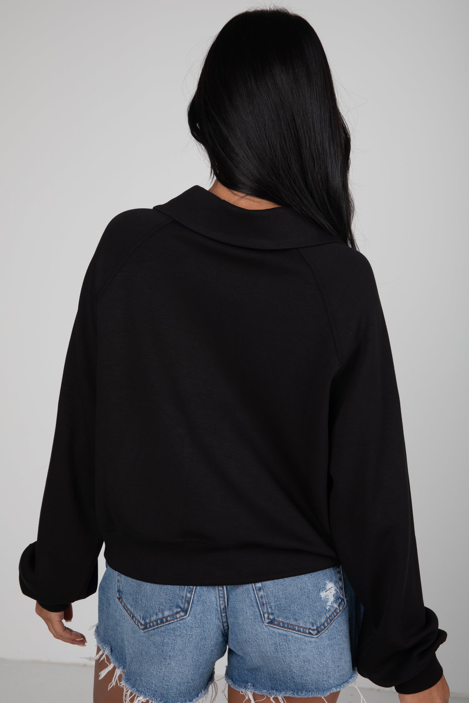 Person wearing a black sweater and denim shorts against a plain background