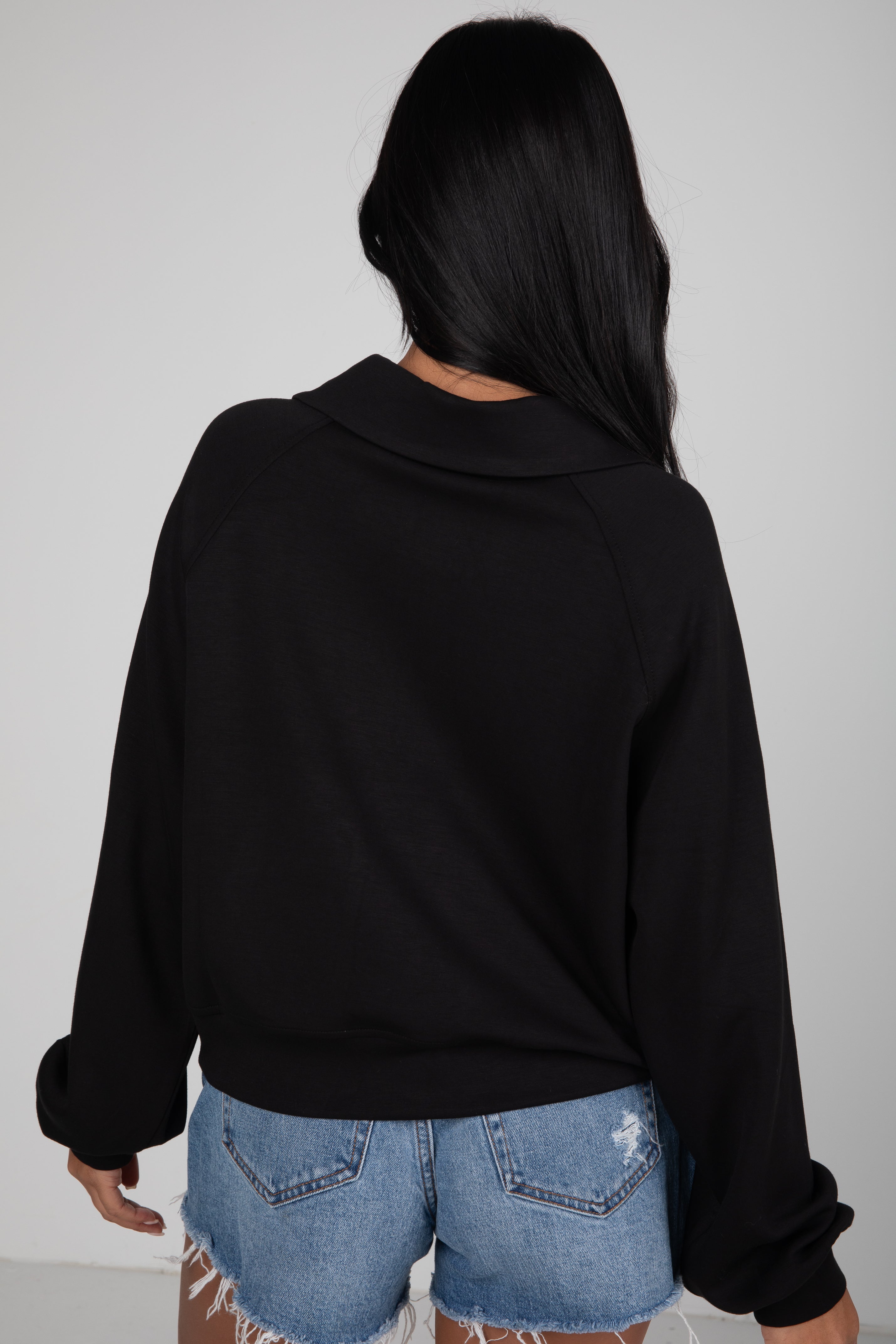 Person wearing a black sweater and denim shorts against a plain background