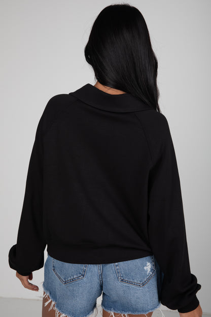 Person wearing a black sweater and denim shorts against a plain background
