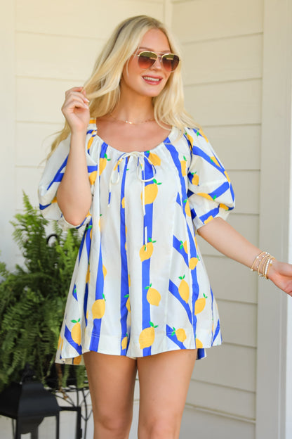 Woman in a colorful dress and white boots standing on a patio with plants and a lantern.