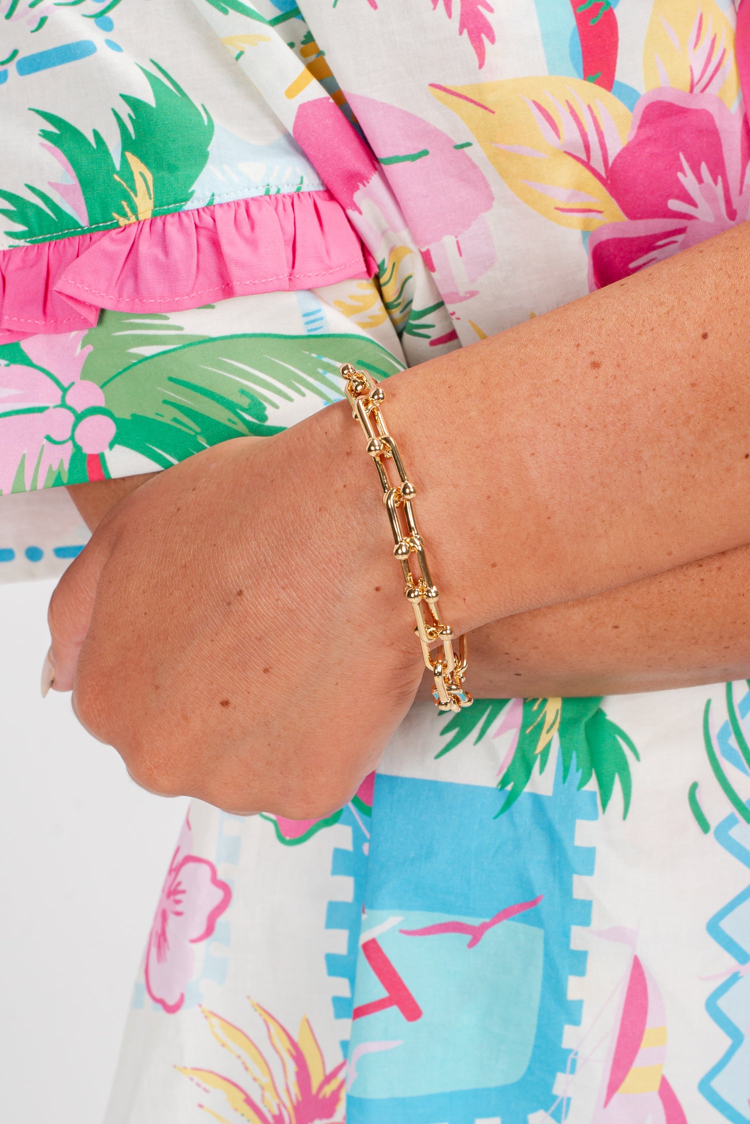 Gold bracelet on a wrist with a colorful tropical-themed dress in the background