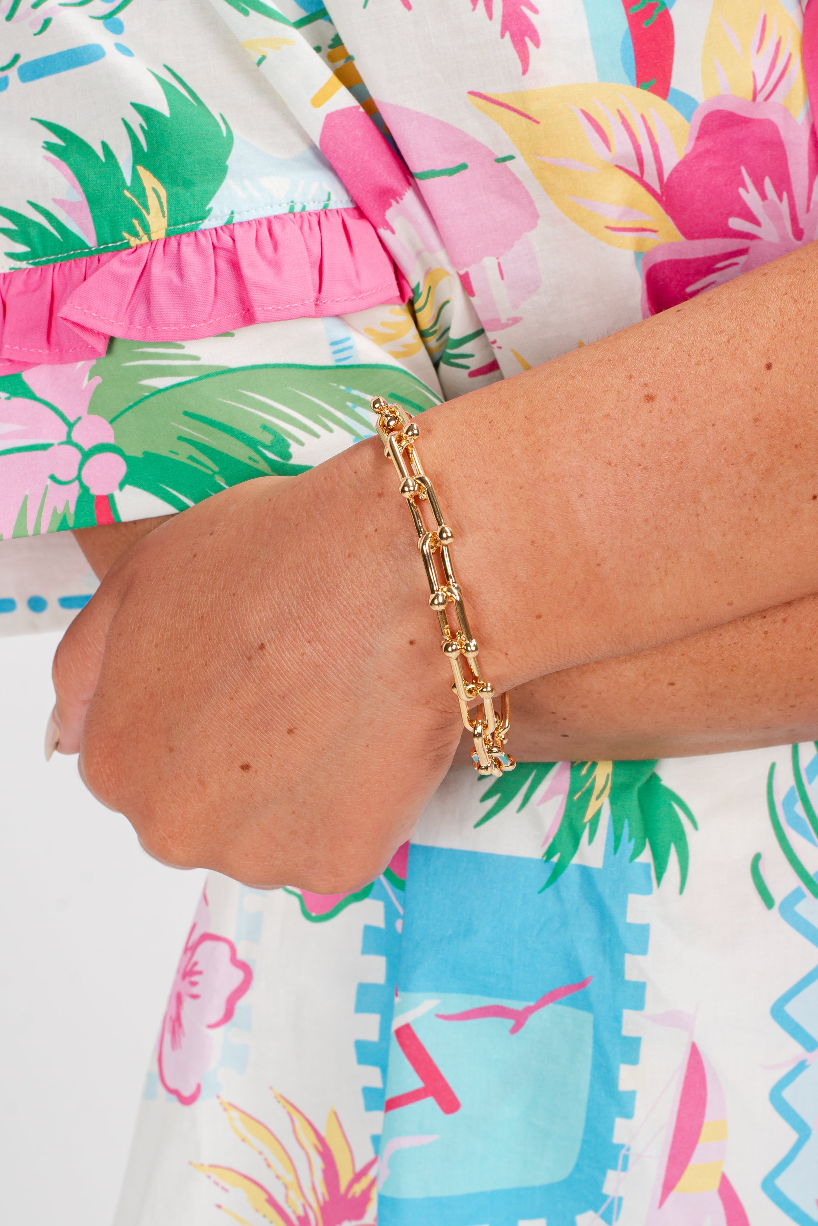 Gold bracelet on a wrist with a colorful tropical-themed dress in the background
