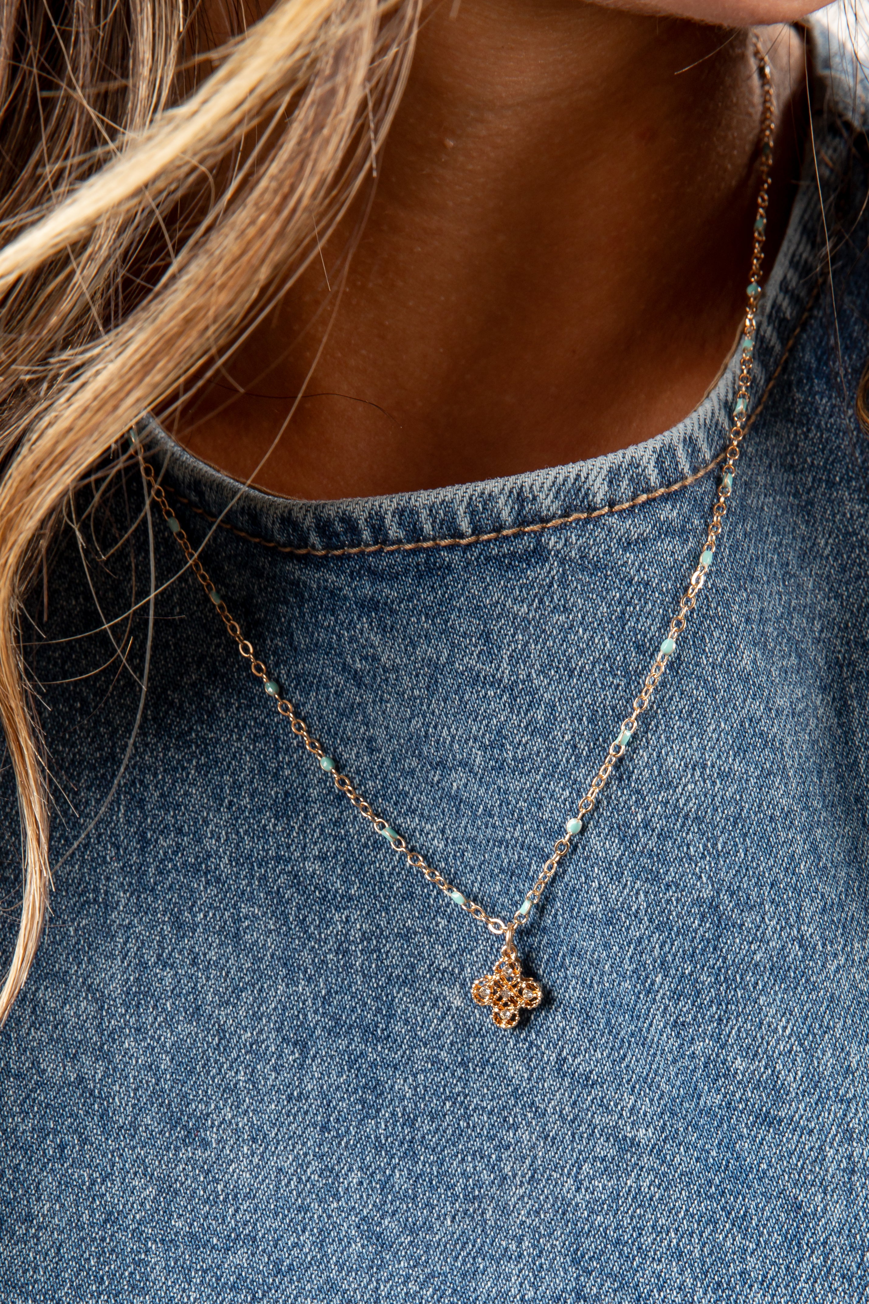 Necklace with a floral pendant worn by a person in a denim shirt
