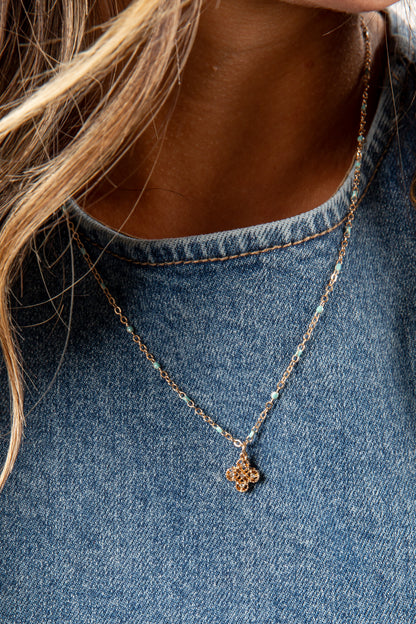 Necklace with a floral pendant worn by a person in a denim shirt