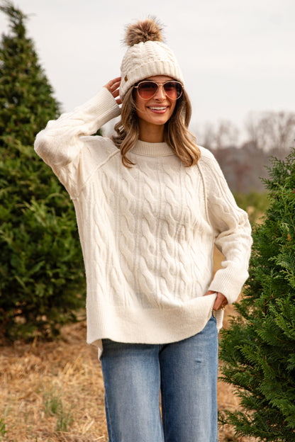 Woman wearing a cream sweater and white beanie in a forest setting