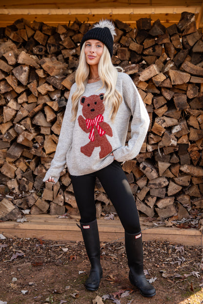 Woman wearing a sweater with a teddy bear design in front of stacked wood.