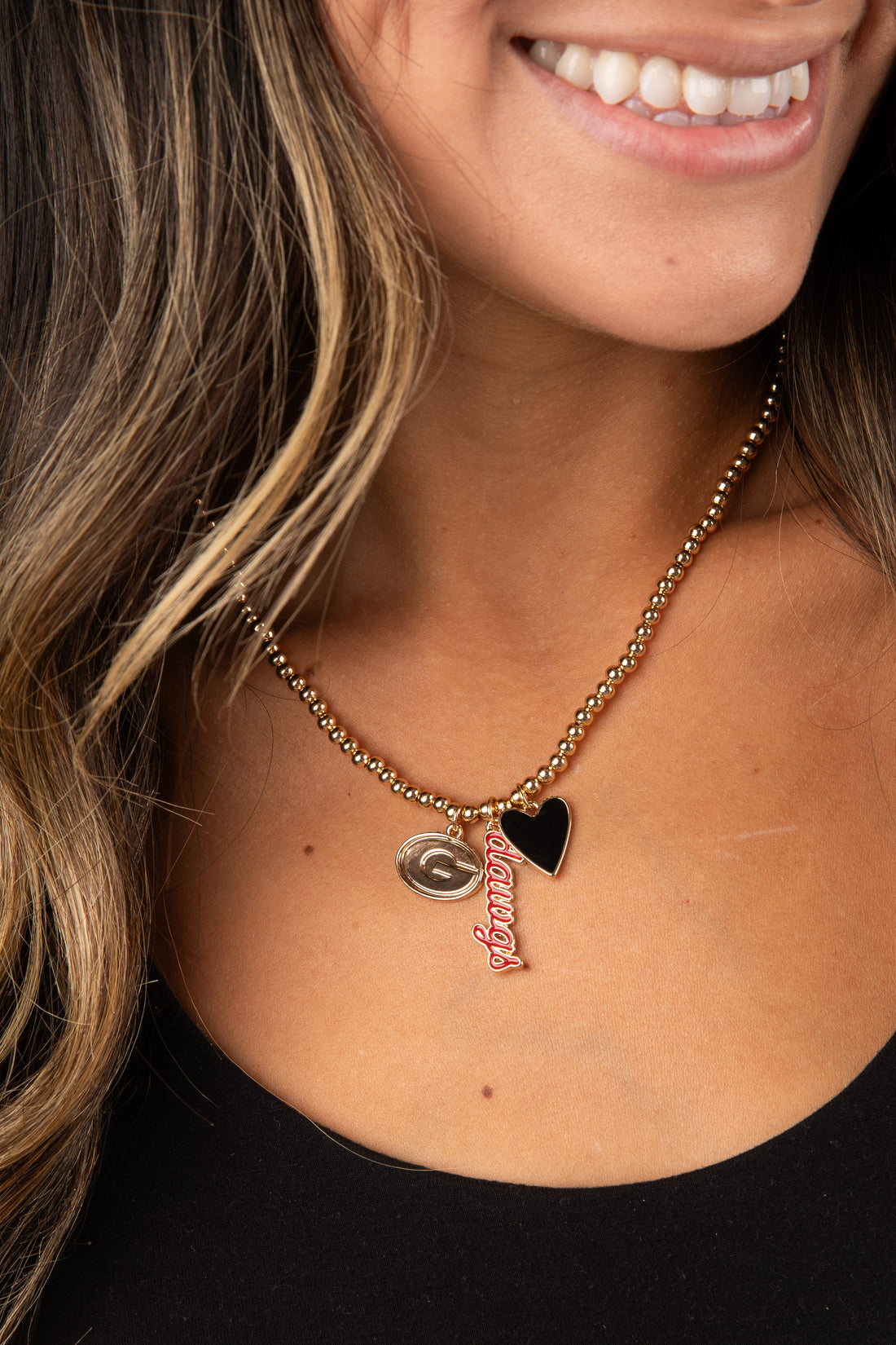 Close-up of a person wearing a gold necklace with a heart pendant and &