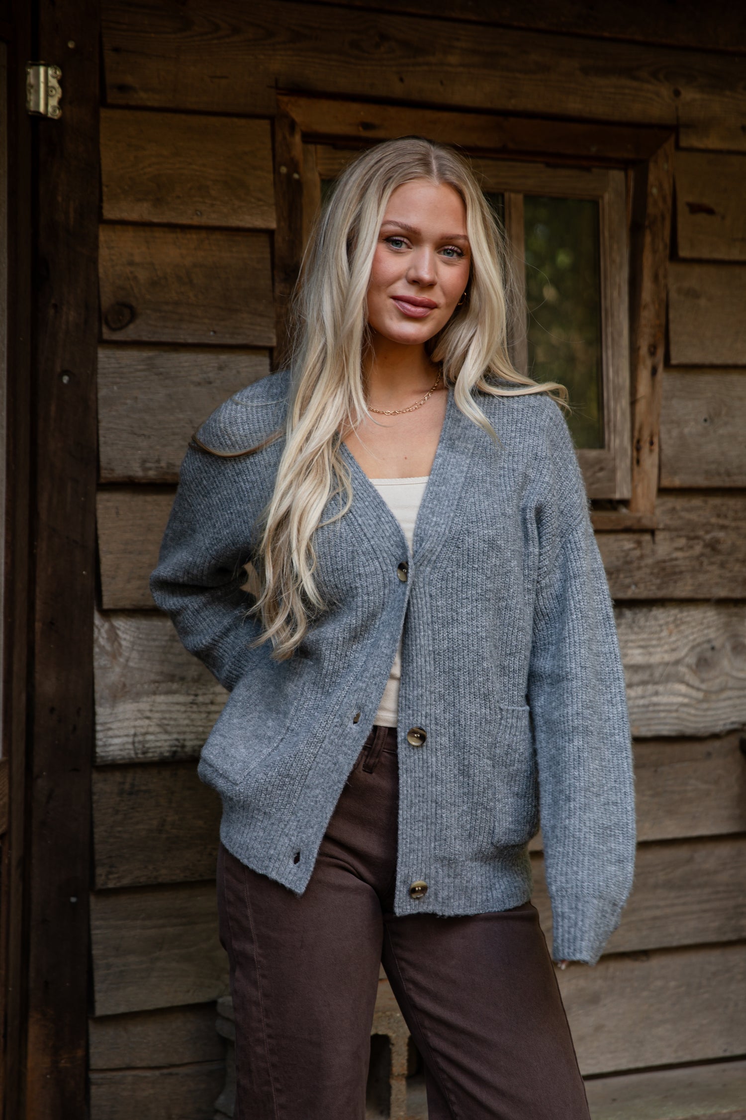 Woman wearing a blue cardigan standing in front of a wooden cabin.