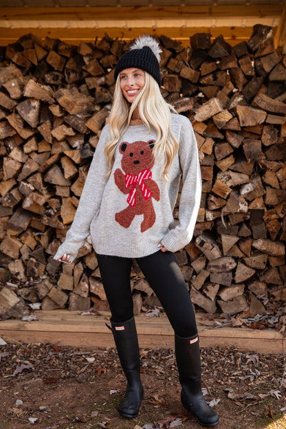 Woman wearing a sweater with a bear design in front of stacked firewood.