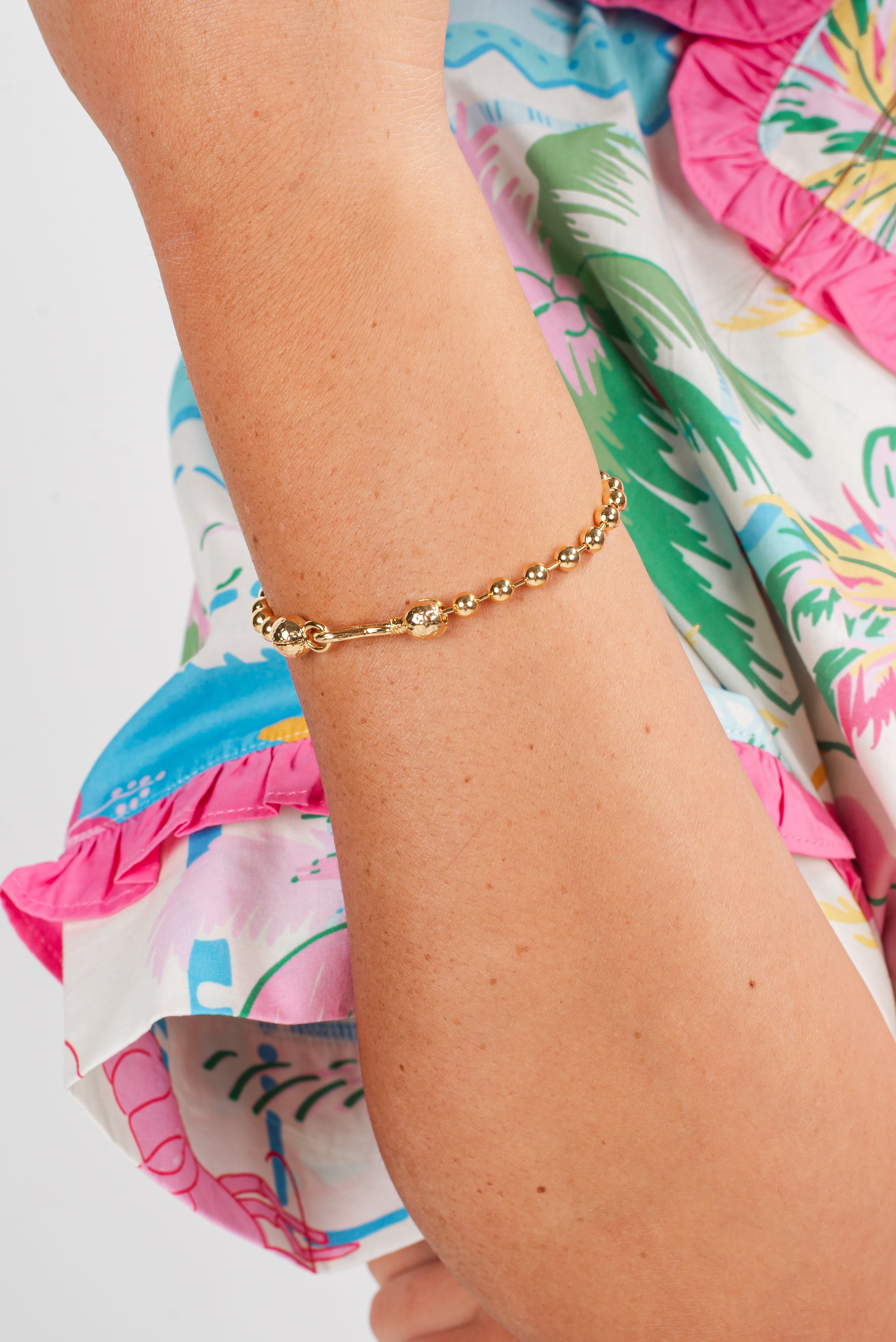 Gold bracelet on a wrist with a colorful, patterned garment in the background