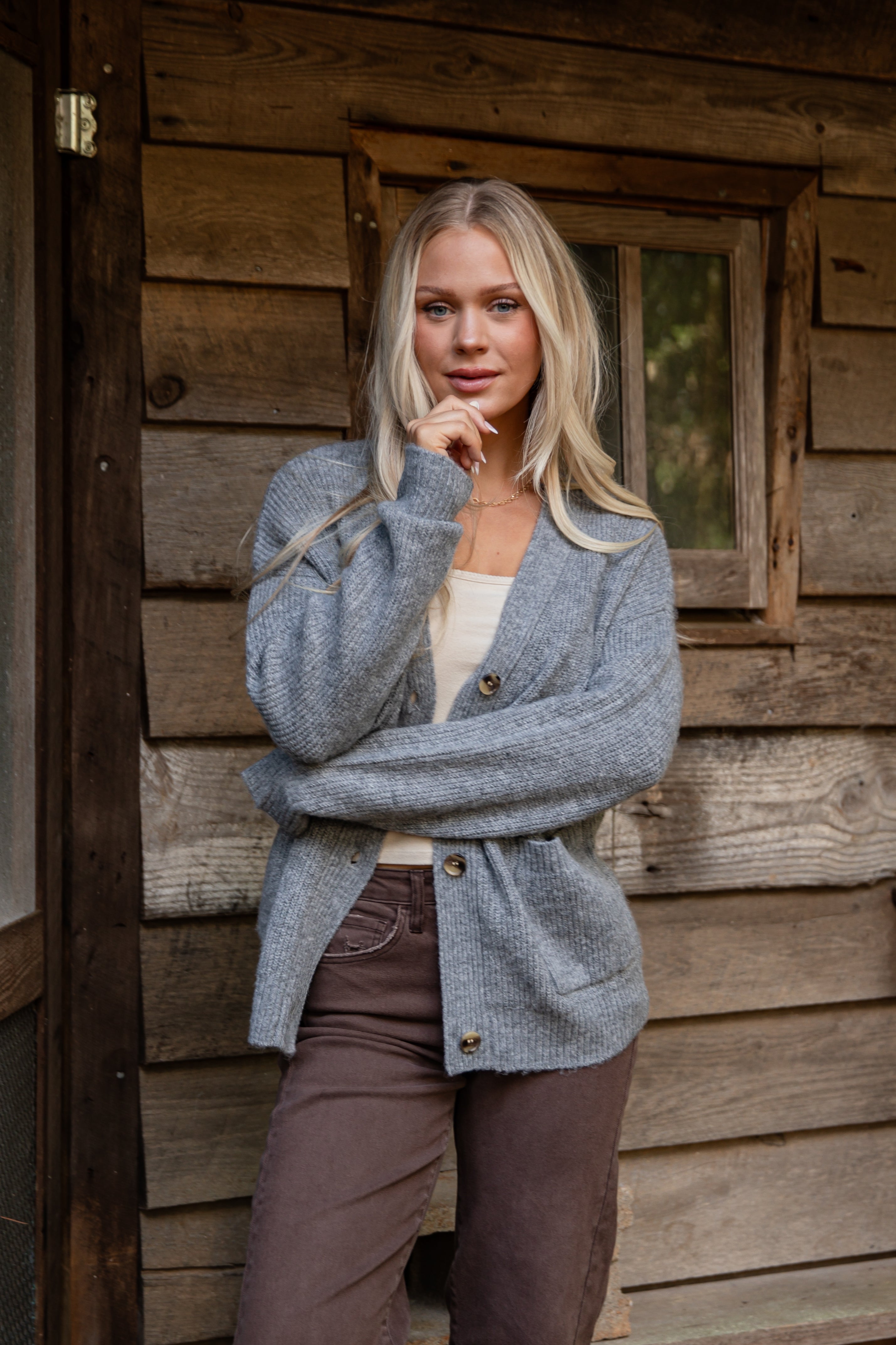 Woman wearing a blue cardigan standing in front of a wooden cabin.