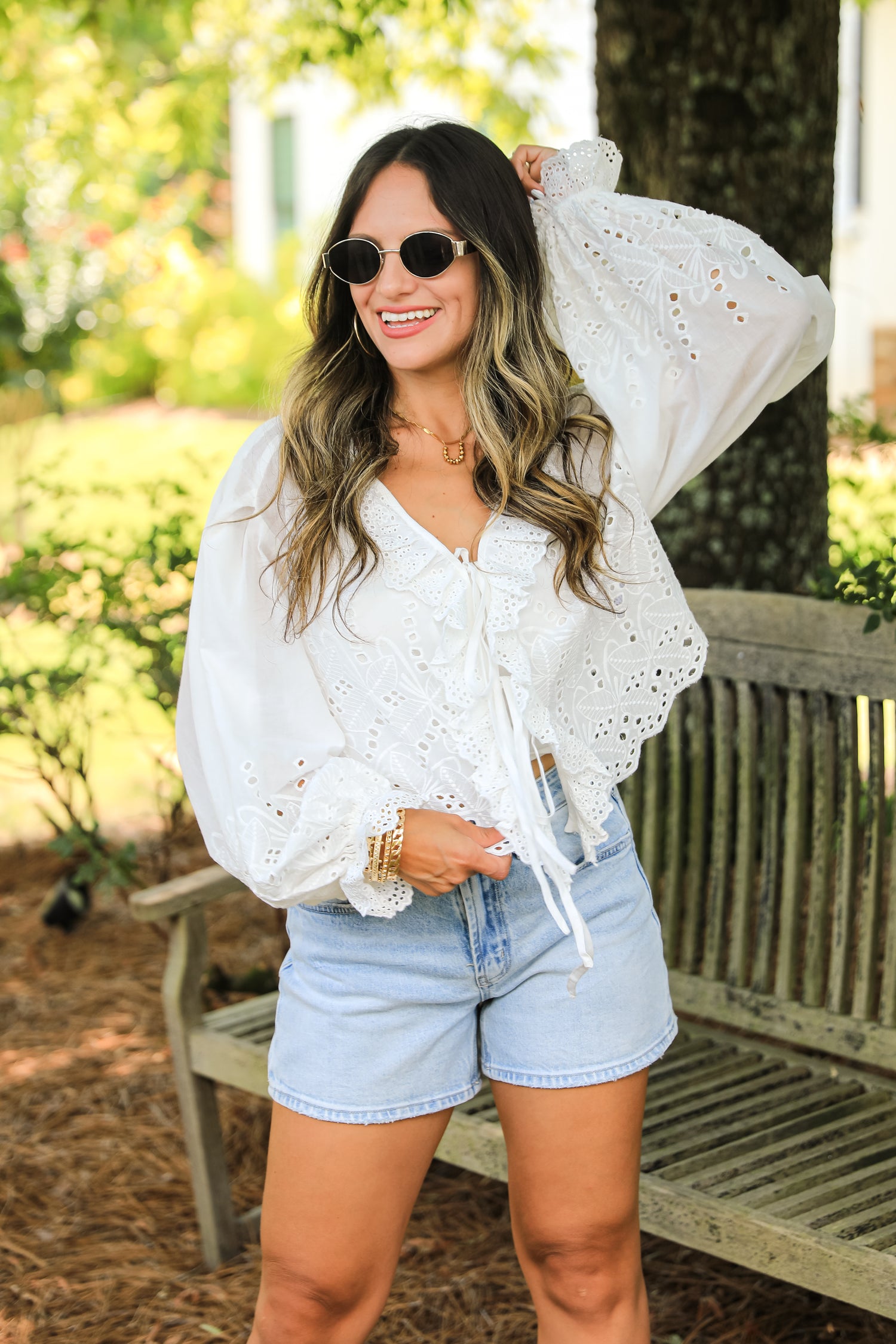 Woman wearing a white lace top and denim shorts outdoors.