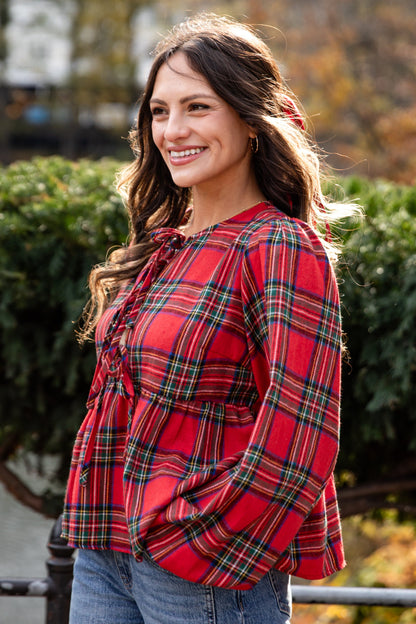 Woman wearing a red plaid shirt in an outdoor setting with trees and foliage.