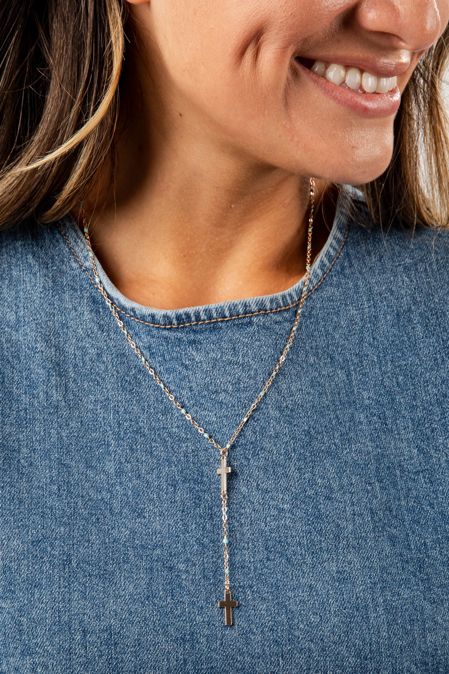 Close-up of a person wearing a necklace with a cross pendant, set against a denim background.