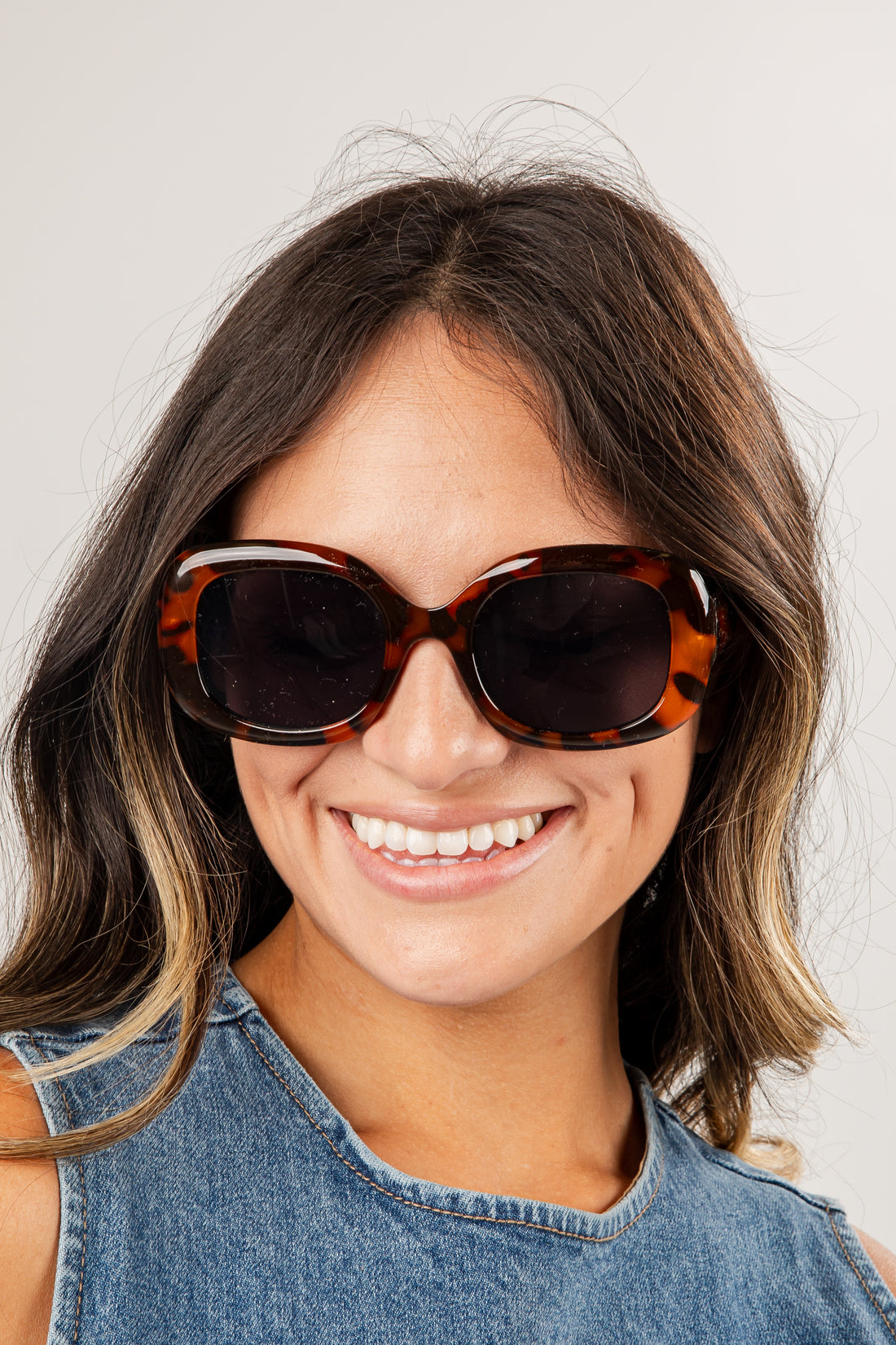 Woman wearing tortoiseshell sunglasses with a plain background