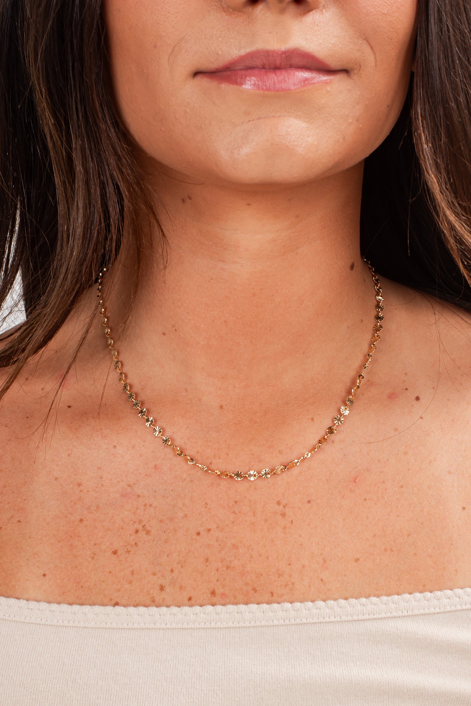 Close-up of a woman wearing a gold necklace with a blurred background