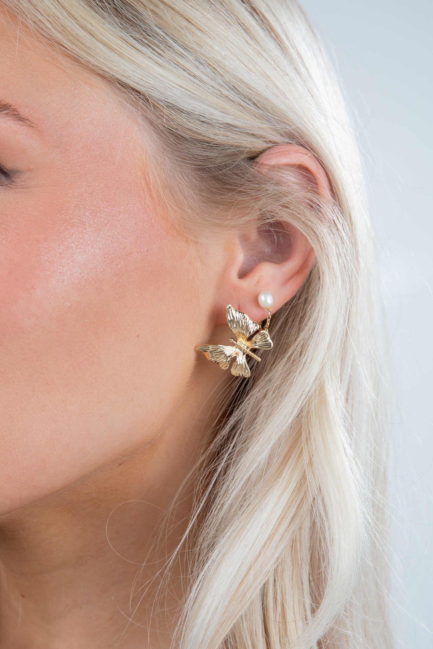 Close-up of a person wearing a gold butterfly earring with a pearl accent.