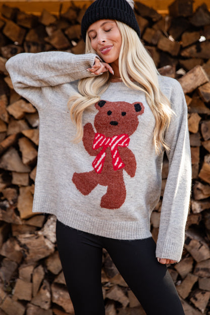 Woman wearing a sweater with a teddy bear design in front of stacked firewood.