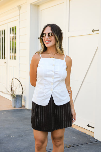 Woman wearing a white button-up top and black pinstripe skirt standing in front of a white door.