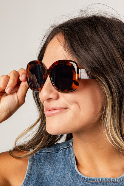 Woman wearing tortoiseshell sunglasses with a neutral background