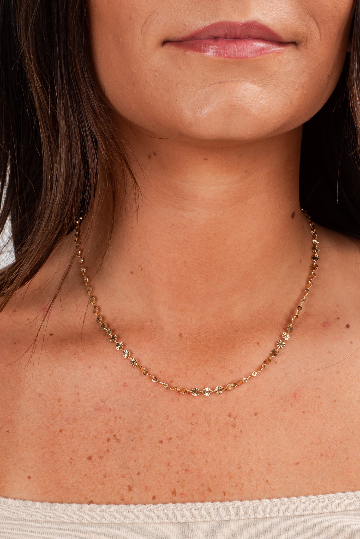 Close-up of a person wearing a gold necklace with a neutral background