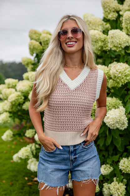 Woman wearing a sleeveless crochet top and denim shorts standing in front of hydrangeas.
