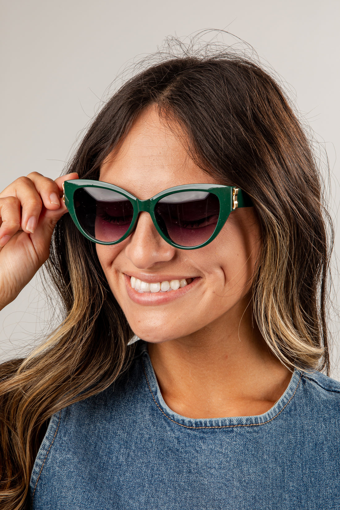 Woman wearing green sunglasses with a neutral background