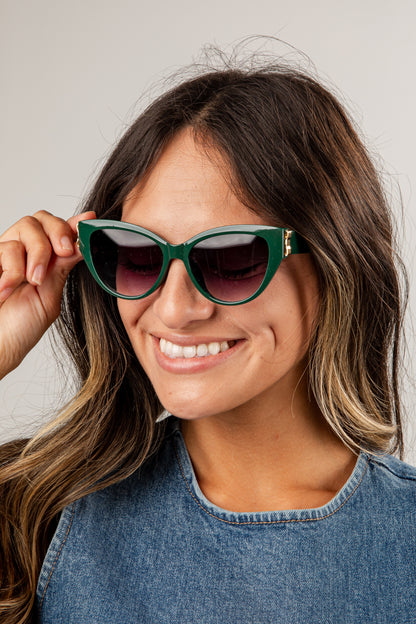 Woman wearing green sunglasses with a neutral background