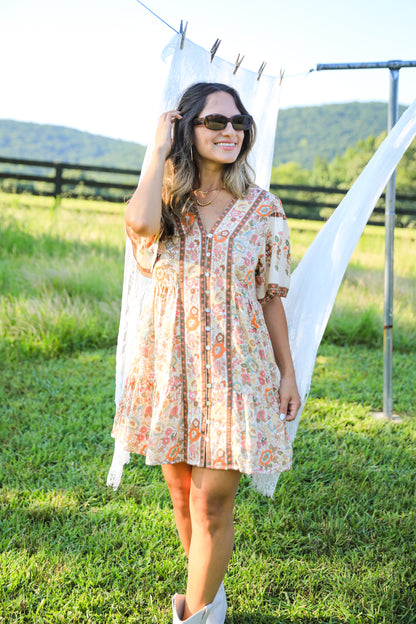 Woman in a floral dress standing in a grassy field with mountains in the background
